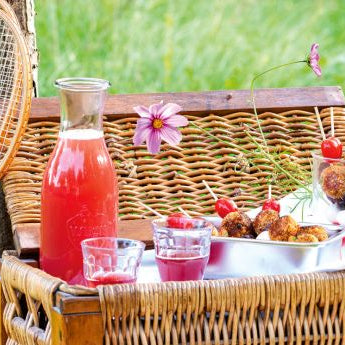 Picknickkorb auf grüner Wiese mit Spießen, Limonade befüllt und angelehnten Tennisschlägern