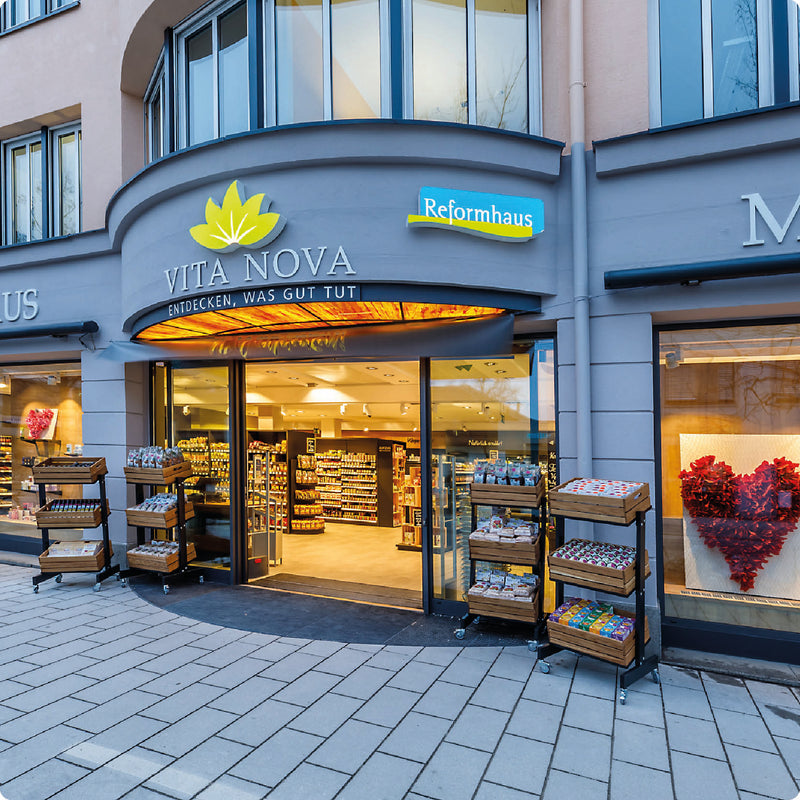 Geöffneter Haupteingang zu der Filiale Vita Nova Reformhaus Mayr in Pasing in abendlicher Stimmung.